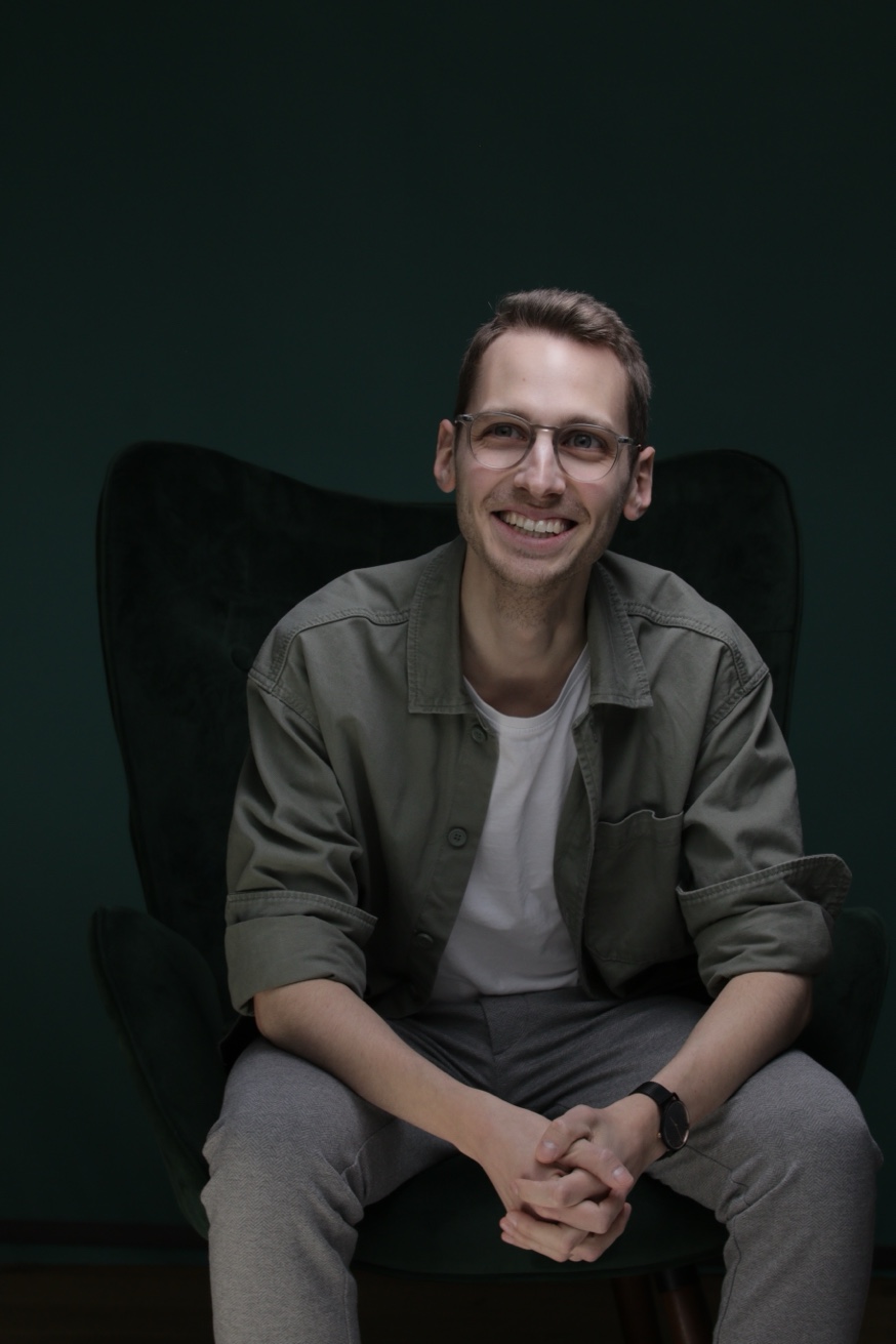Portraitfoto von Phil Rieger, lächelnd auf einem dunkelgrünen Sessel sitzend